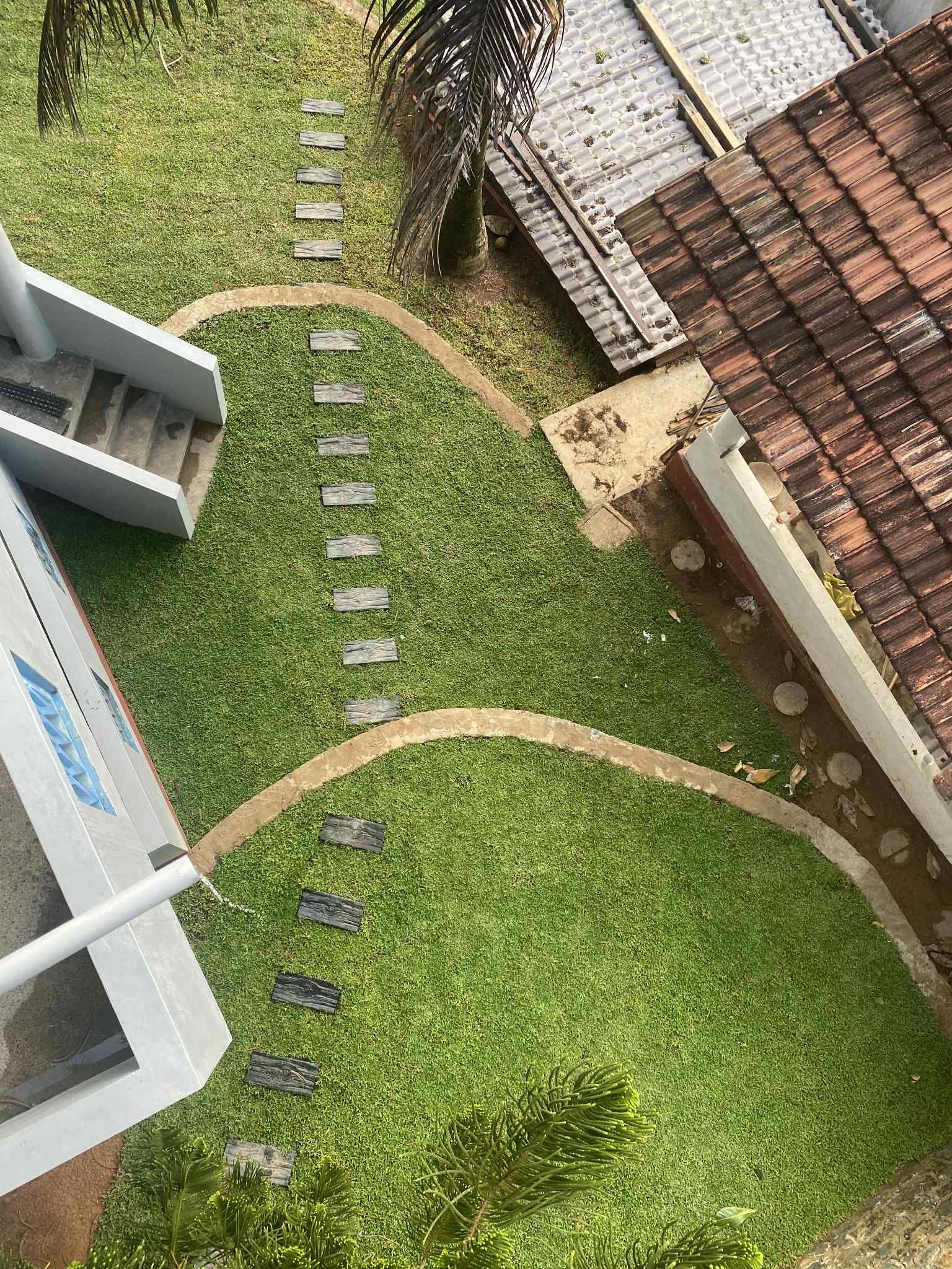 Overhead view of a grassy yard with stepping stones, winding pathways, and two buildings.