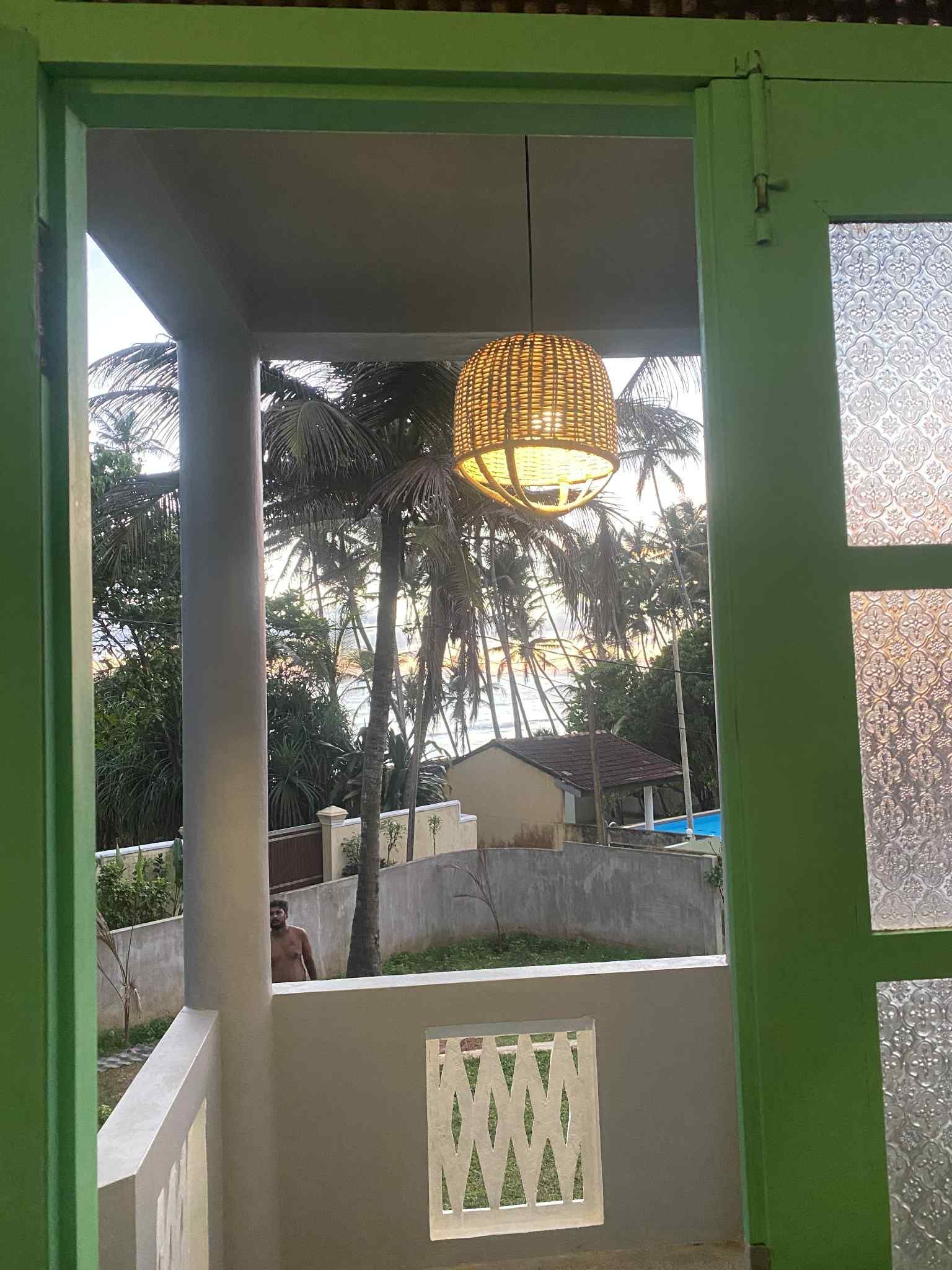 Green door frame looking out to a balcony with a hanging light. Trees and a building are visible in the distance.