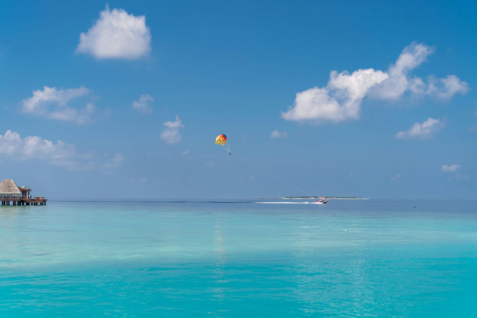 Bright turquoise ocean under a blue sky with scattered clouds. A parasailer and boat are visible.