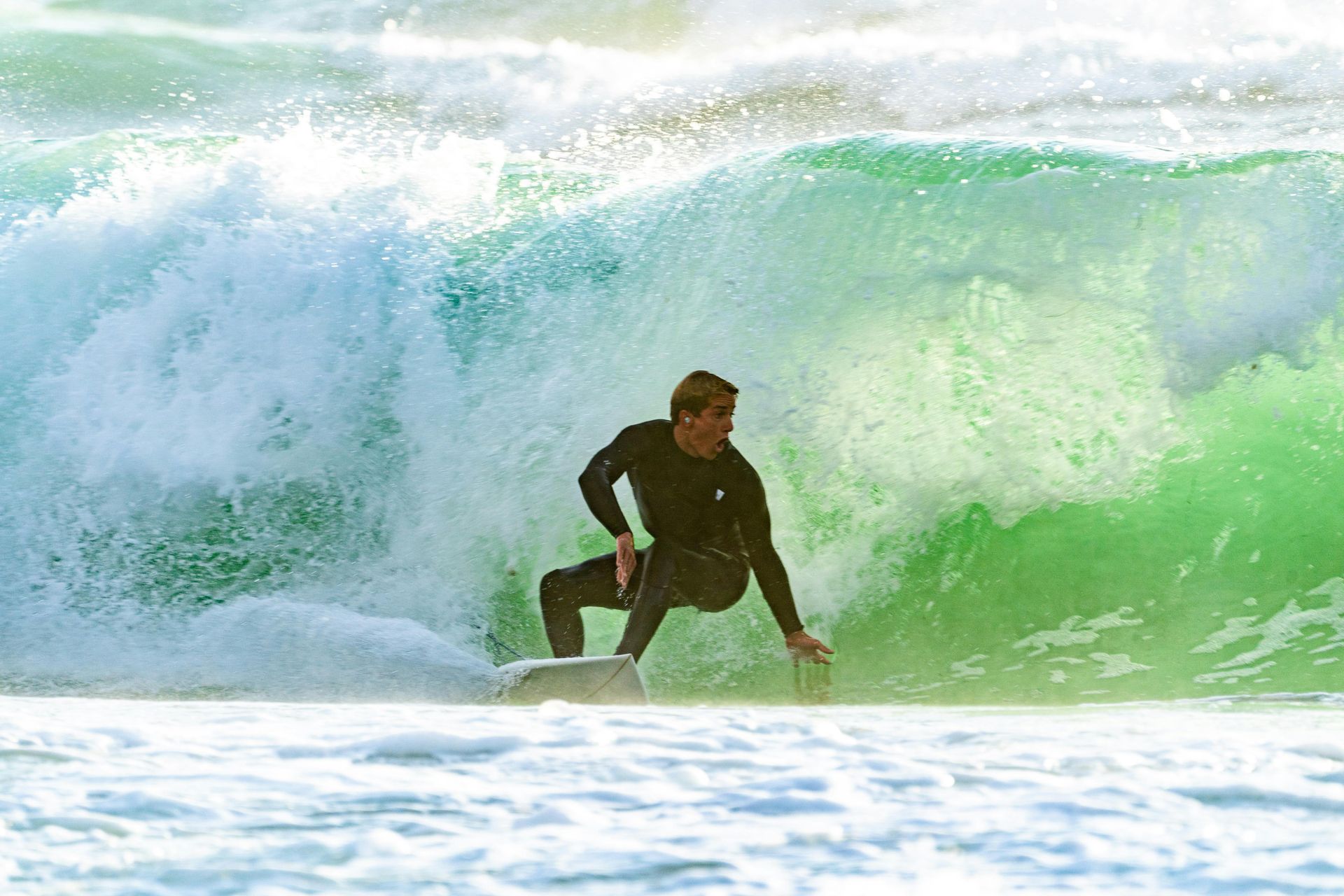 Surfer in black wetsuit rides a green wave, balancing on board, ocean setting.