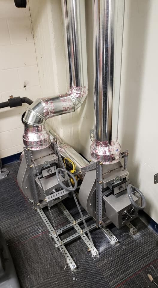 Two silver HVAC units with ductwork. Units are on metal shelving.