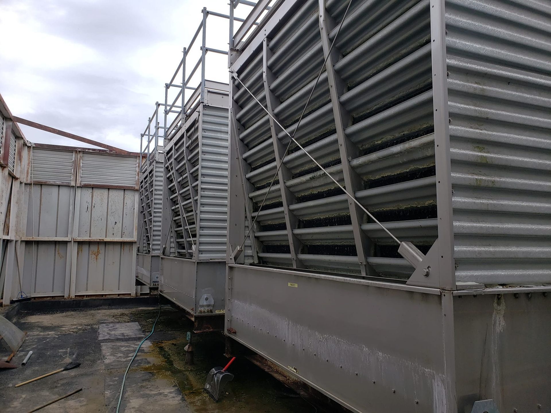 Cooling towers on a rooftop. Gray metal structures with slatted sides under a cloudy sky.