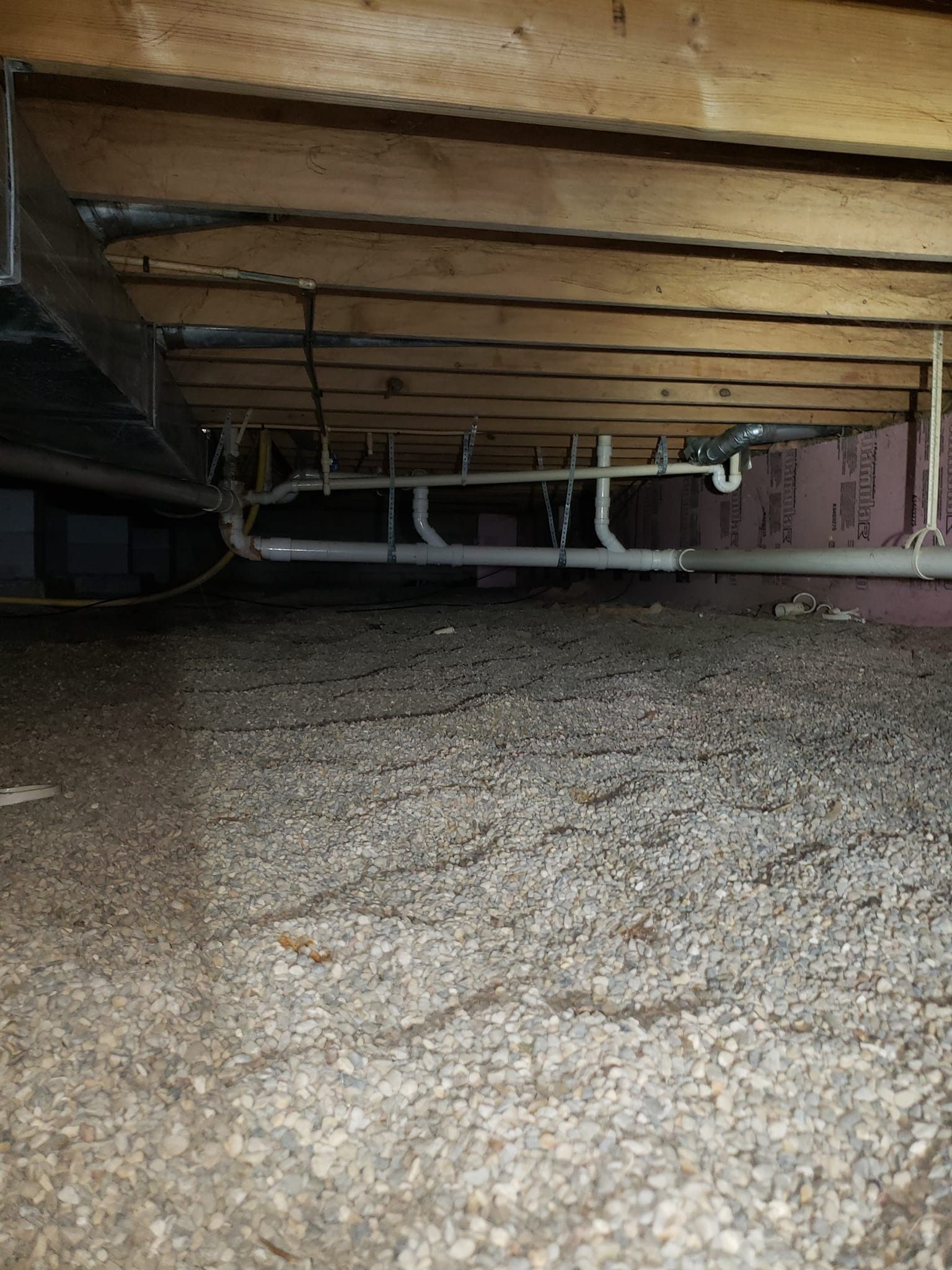 Underneath a house: exposed joists, pipes, gravel ground.