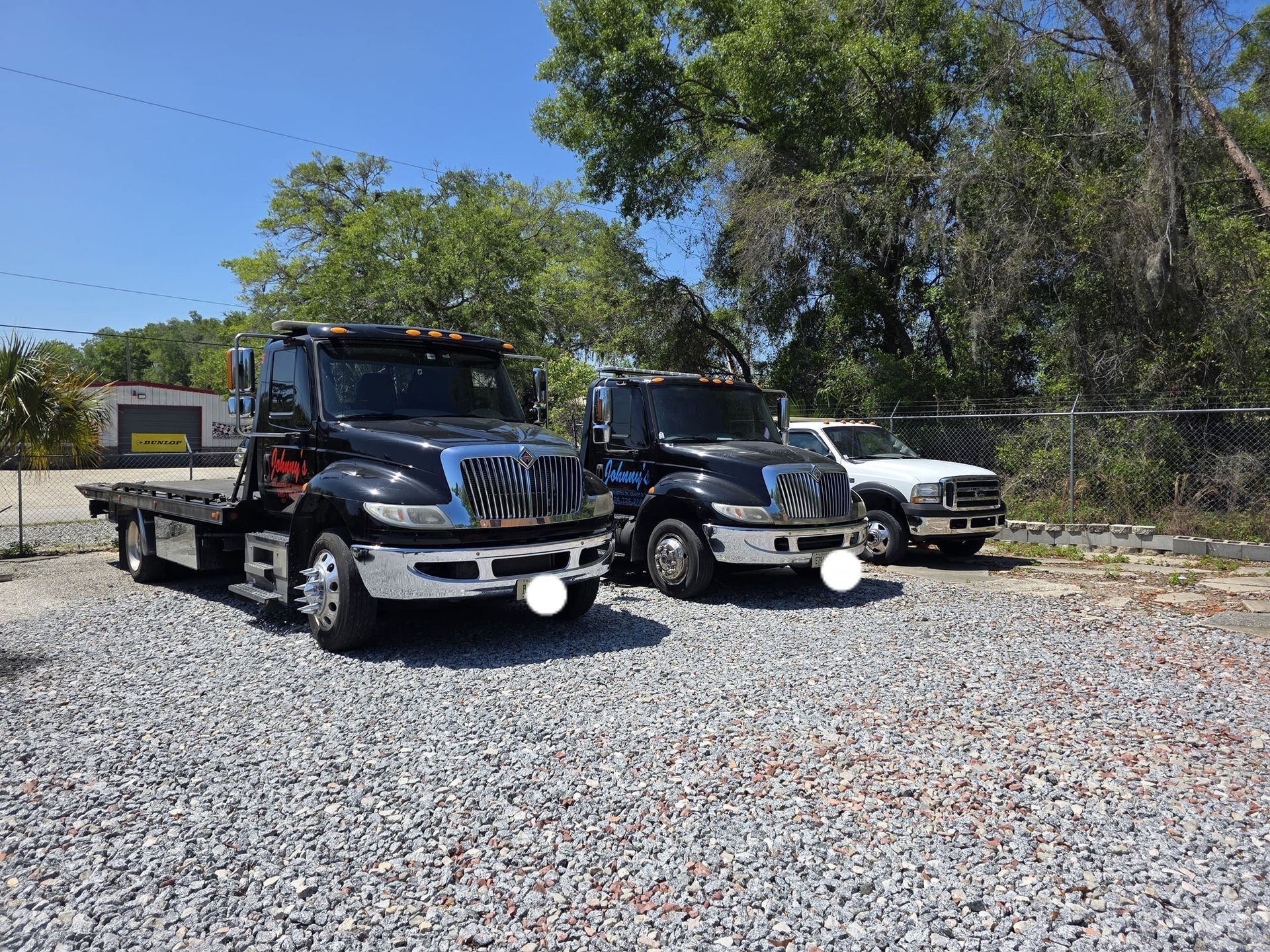 Three tow trucks parked on gravel under a blue sky with trees in the background.