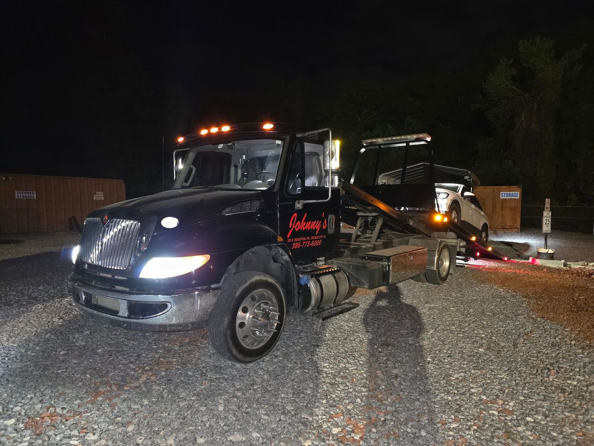 Black tow truck loading a car at night on gravel. 
