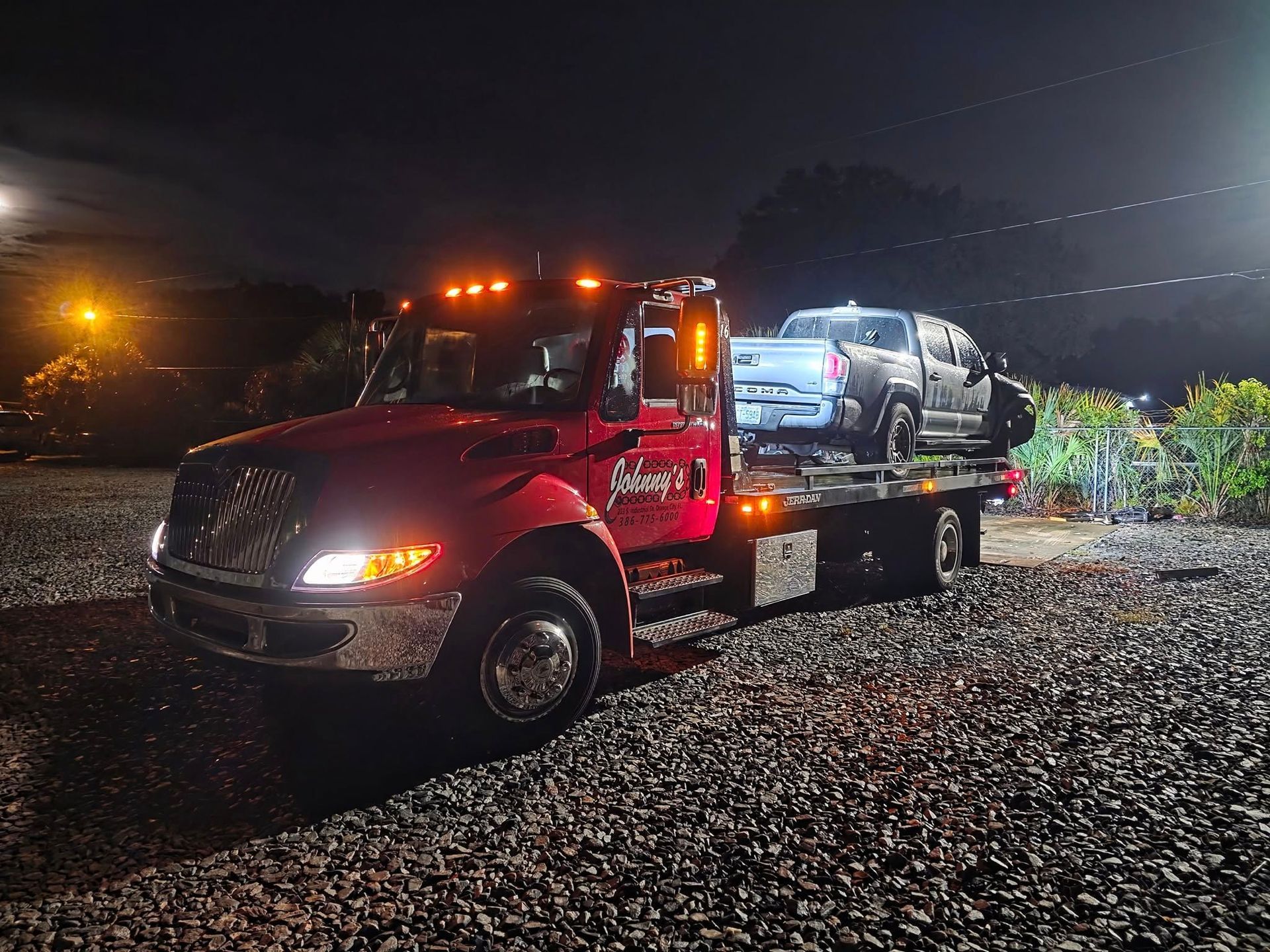 Red tow truck with a pickup truck on its flatbed, at night.