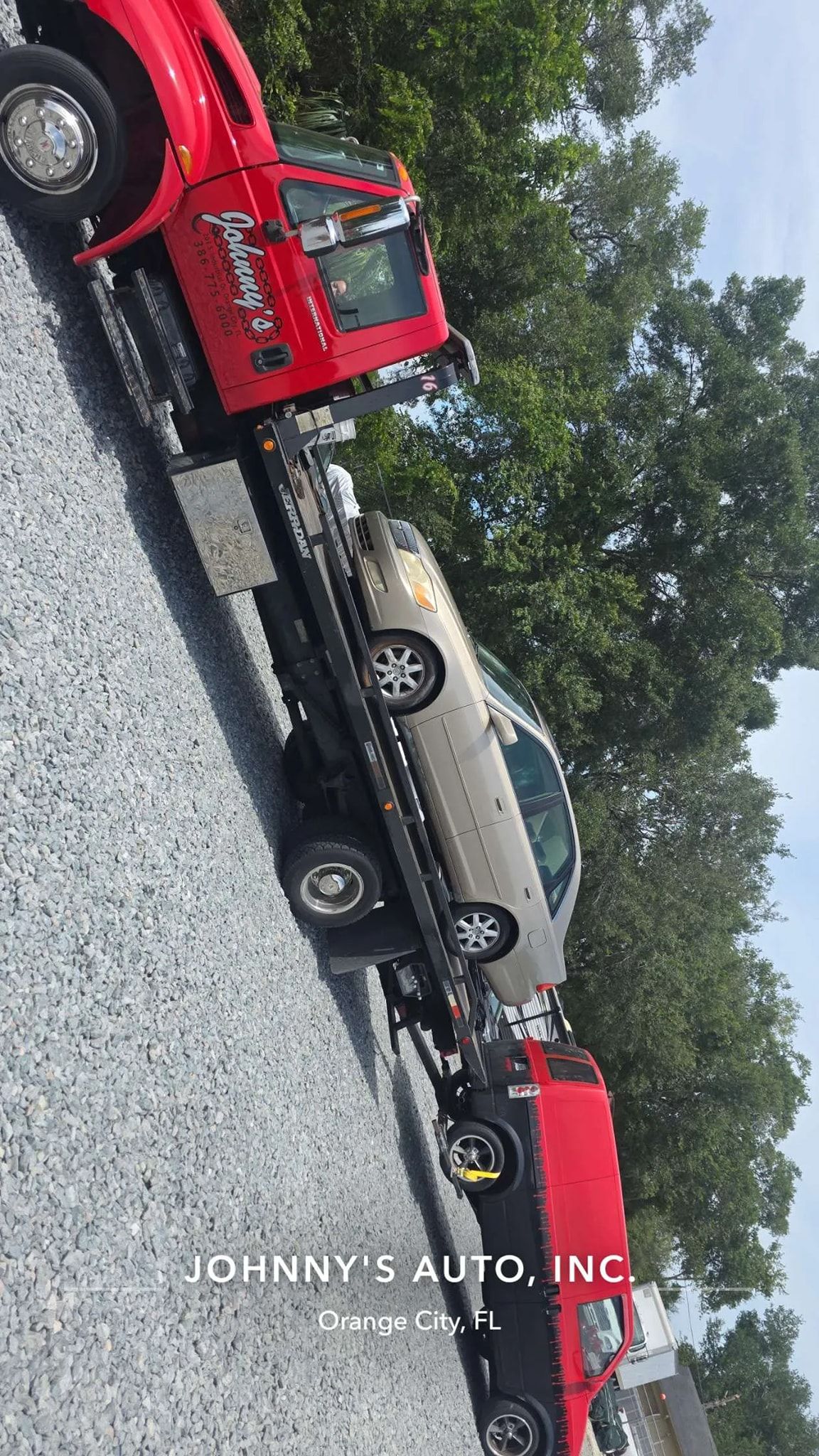 Red tow truck carrying a tan car on a flatbed.
