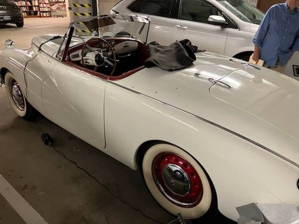 A man is standing next to a white convertible car in a parking garage.