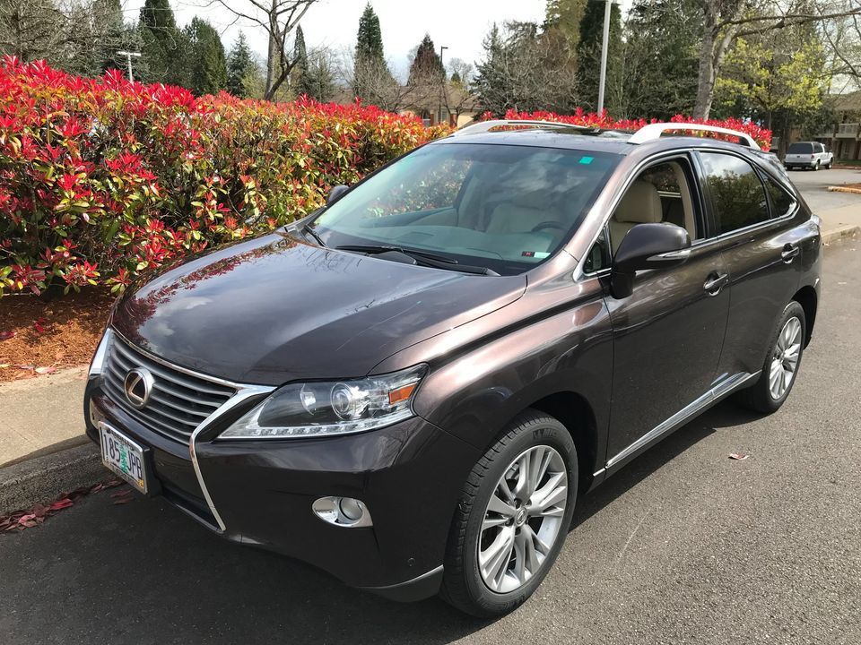 A black lexus is parked on the side of the road in front of a bush.