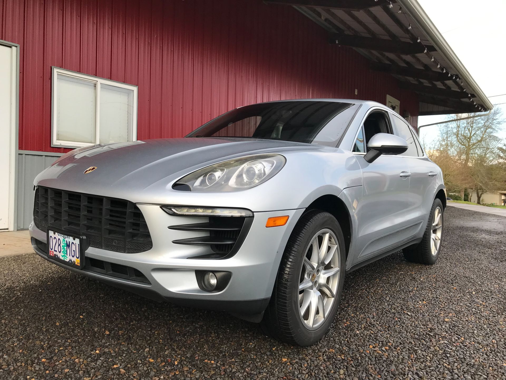 A silver porsche macan is parked in front of a red building.