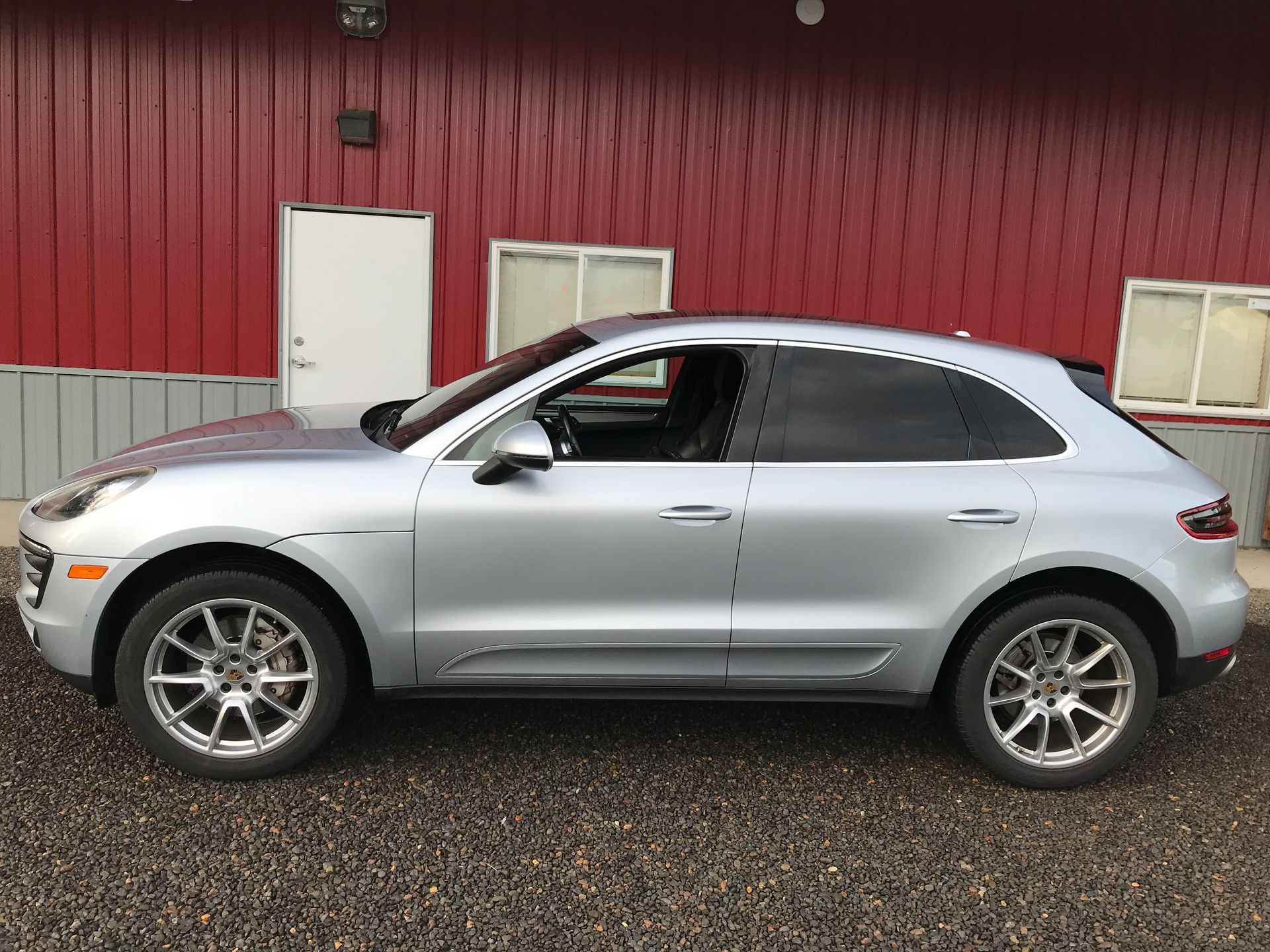 A silver porsche macan is parked in front of a red building.