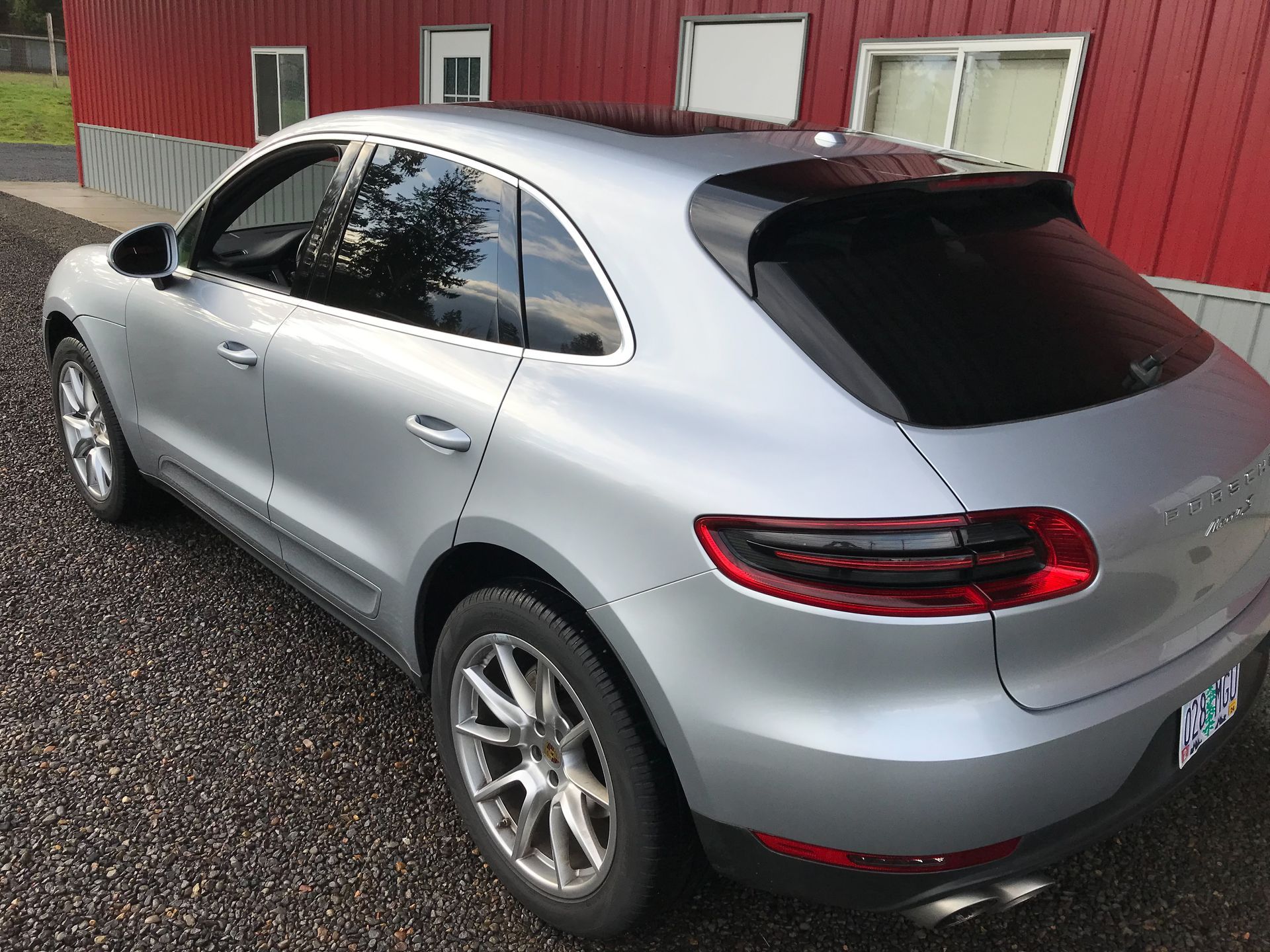 A silver porsche macan is parked in front of a red building.
