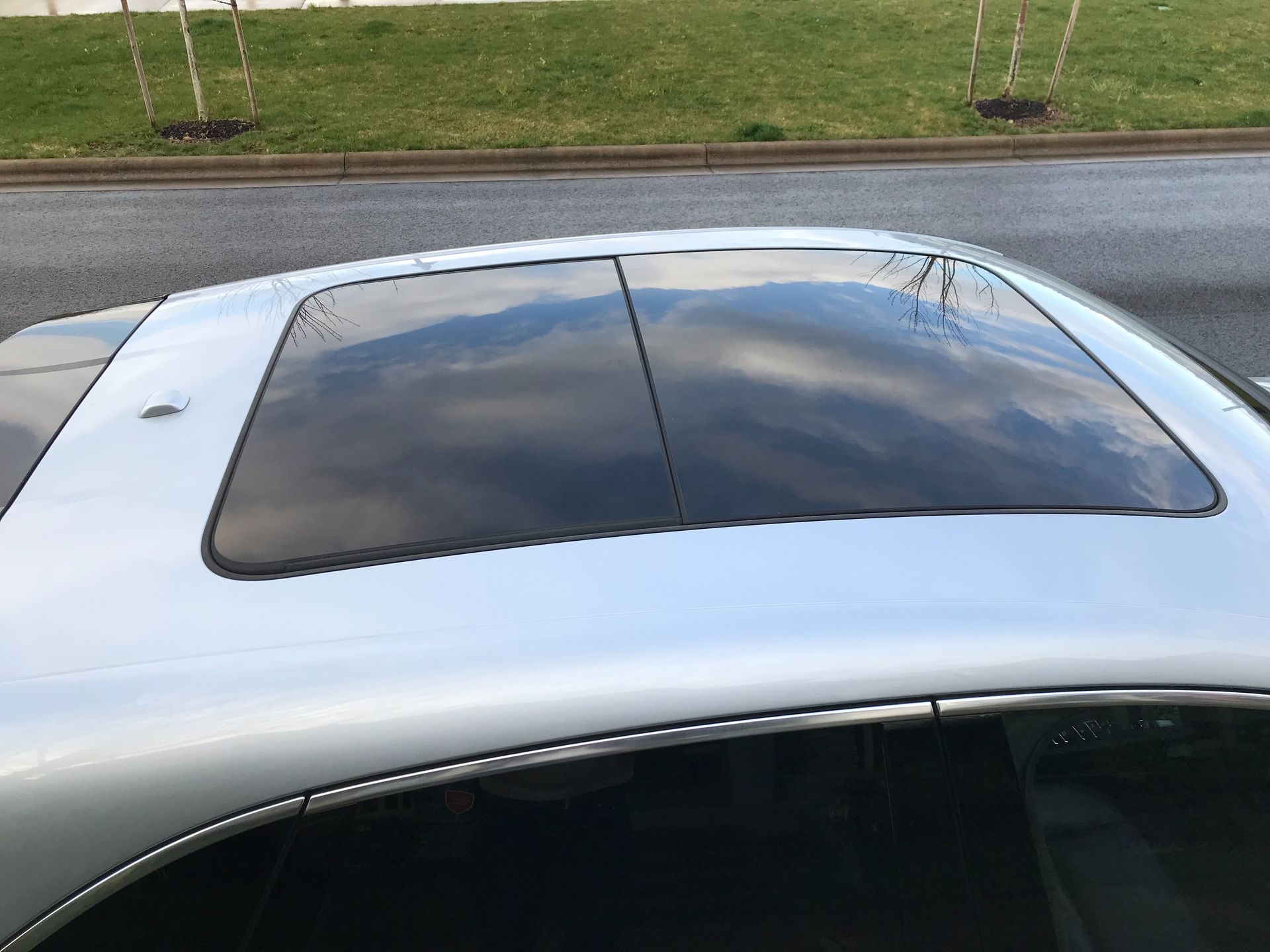 A silver car with a sunroof is parked on the side of the road.