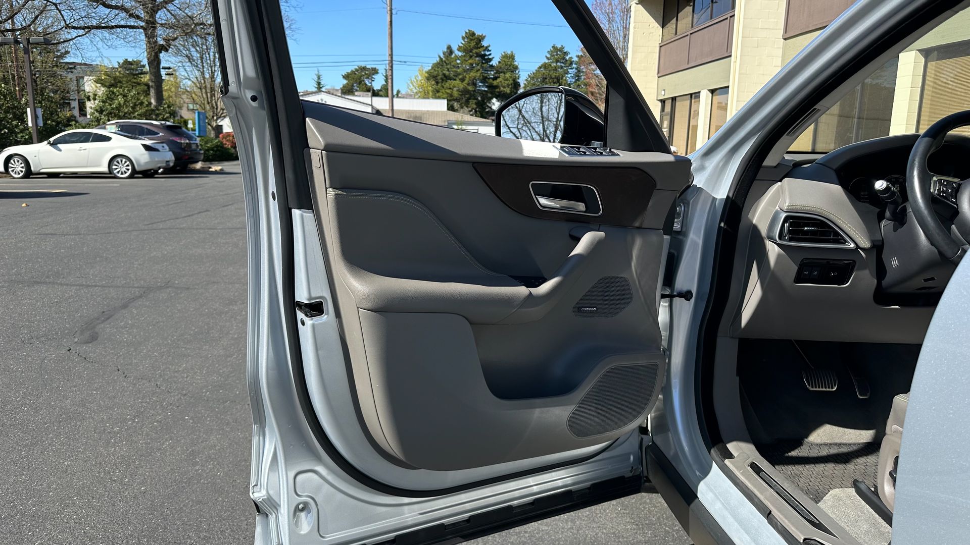 A silver car with the door open is parked in a parking lot.