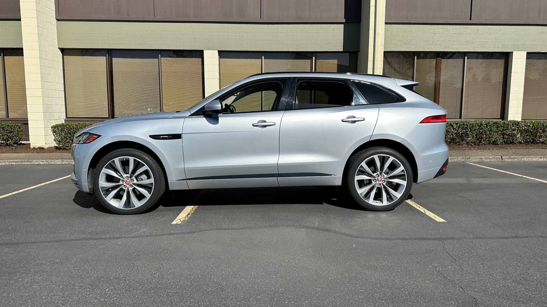 A silver jaguar f pace is parked in a parking lot in front of a building.