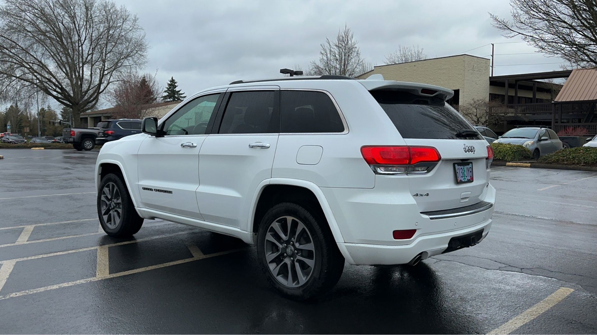 A white jeep grand cherokee is parked in a parking lot on a rainy day.