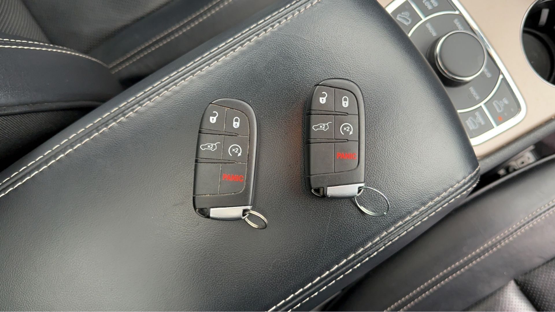 Two remote keys are sitting on the arm rest of a car.