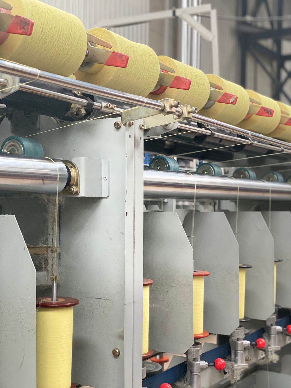 Una fila de carretes de hilo amarillo están colocados sobre una cinta transportadora en una fábrica.