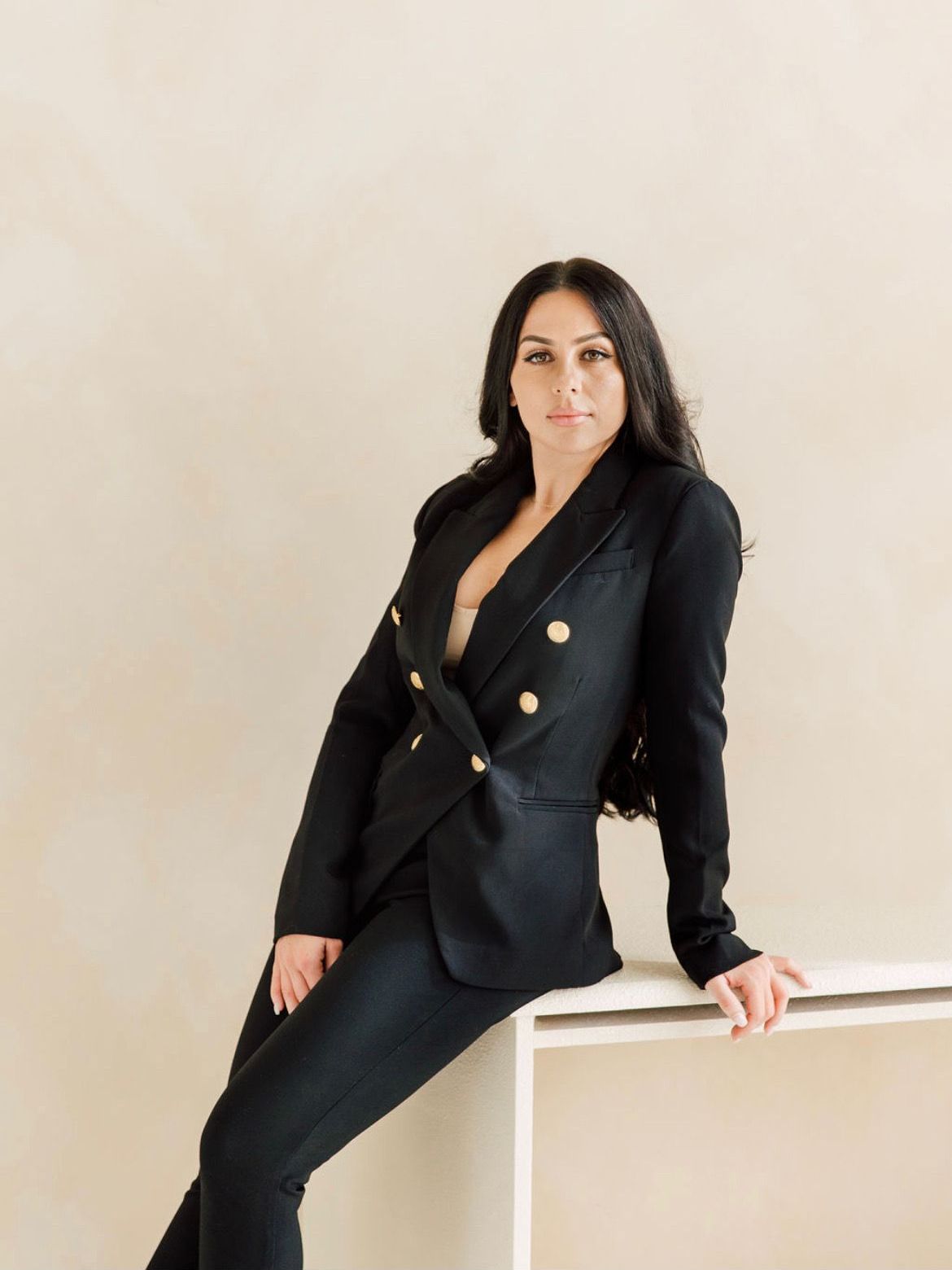 A woman in a black suit is sitting on a white table.