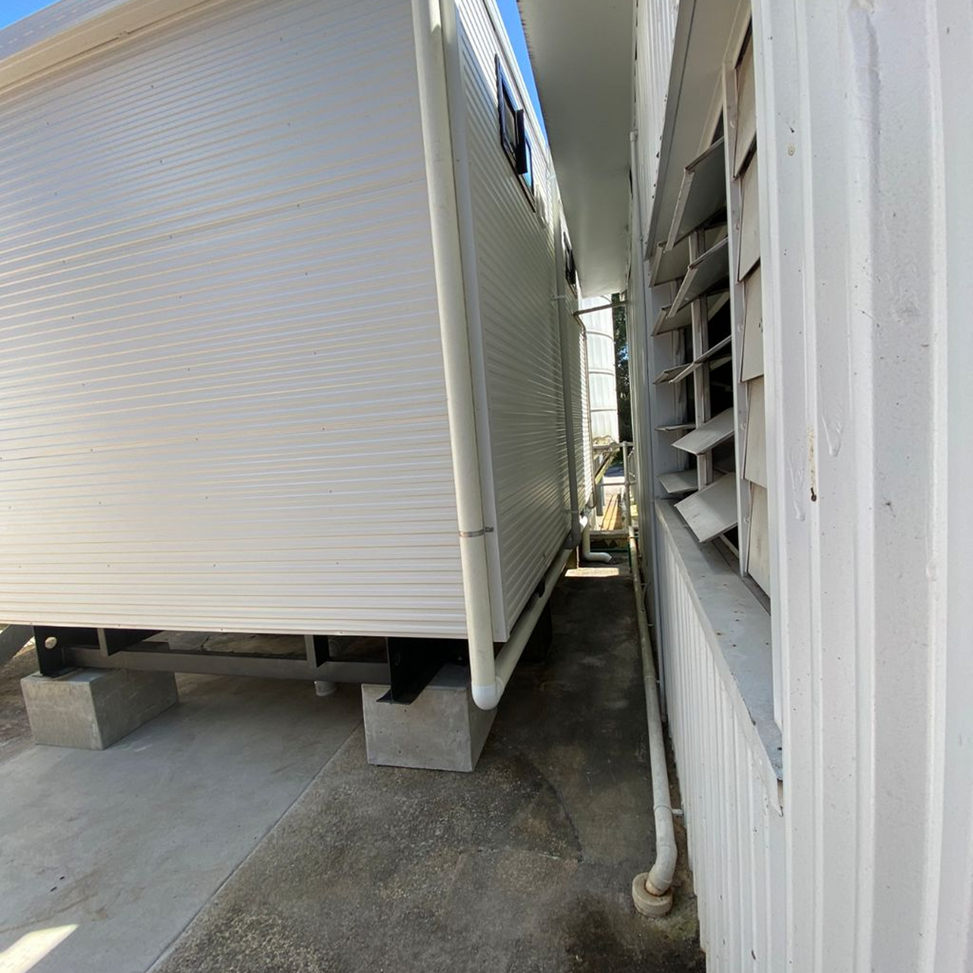 White buildings with a narrow walkway. One building has shutters; the other has a roll-up door.