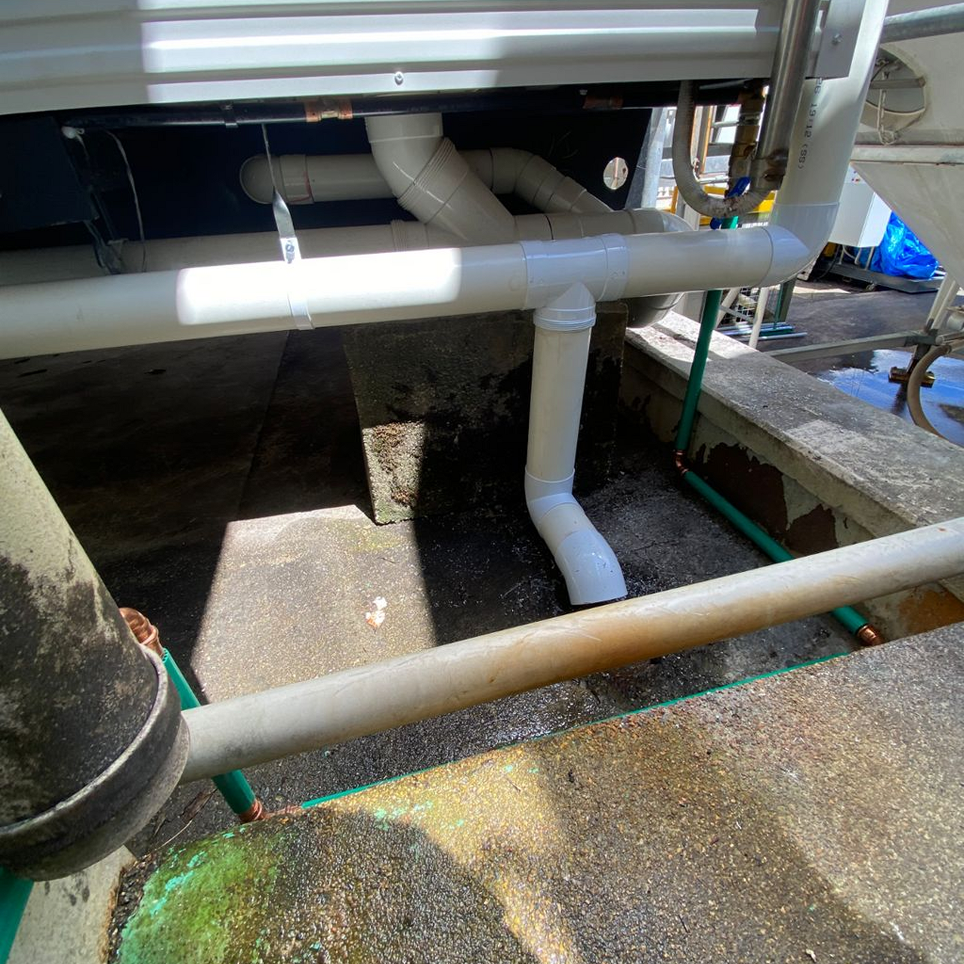 White PVC pipes connected to machinery in an outdoor setting, with some water present.