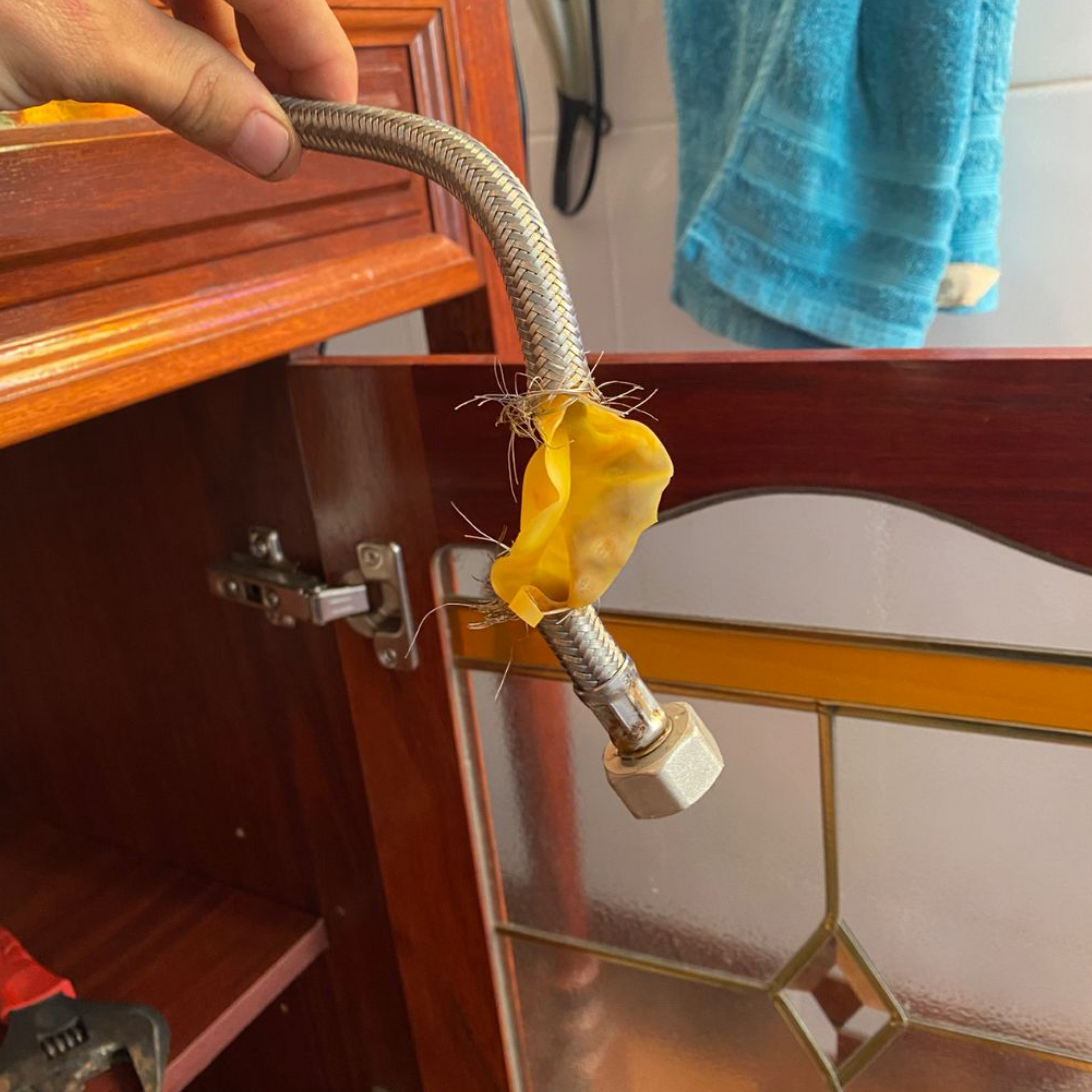 A hand holding a silver flexible water hose with a yellow, fibrous substance attached, near a cabinet.
