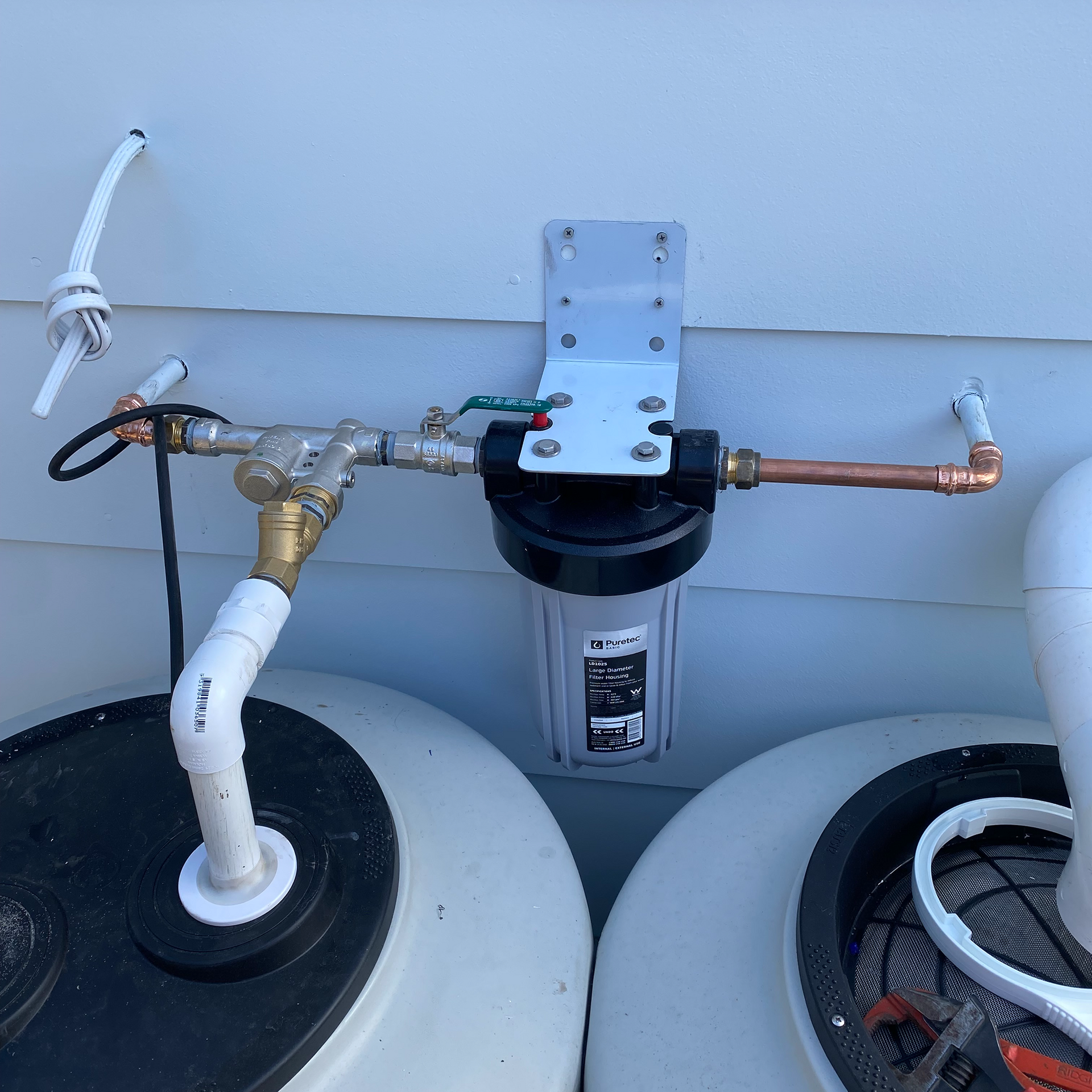 Water filtration system mounted on a wall, connected to tanks via pipes.