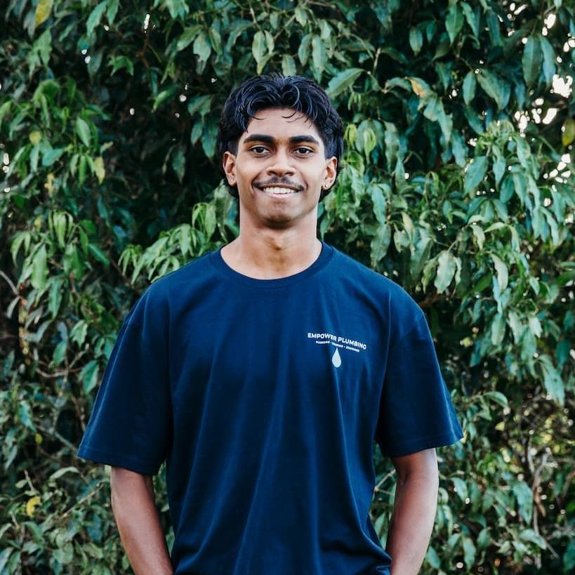 Man in a blue shirt smiles in front of green foliage.