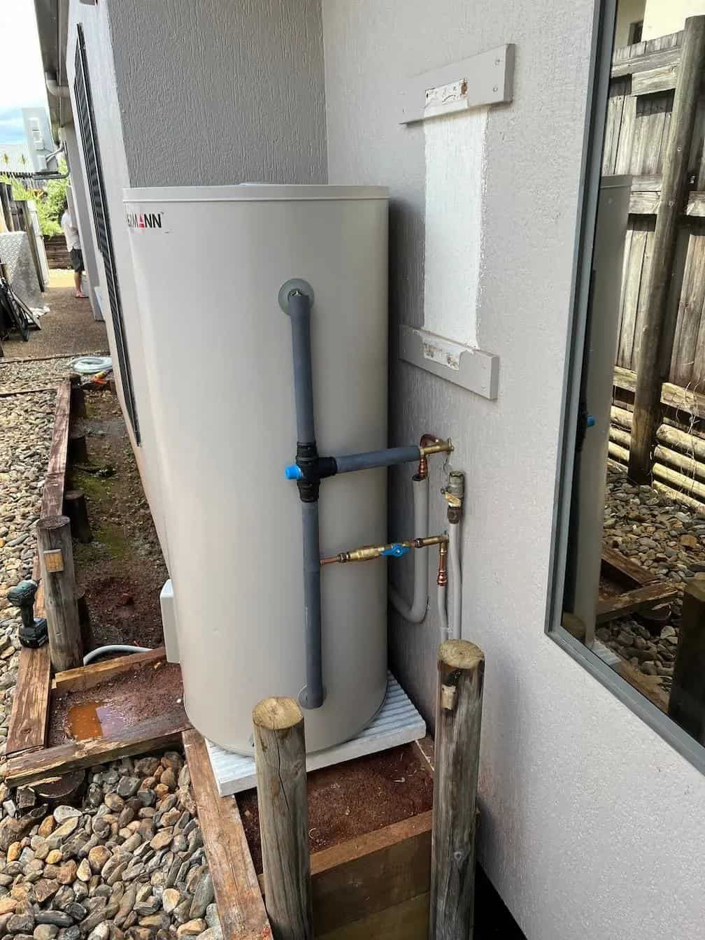 Heat pump water heater installed outside a building next to a window and wooden posts.