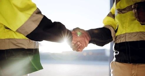 Person wearing gloves handles a pane of glass in an orange workshop setting.