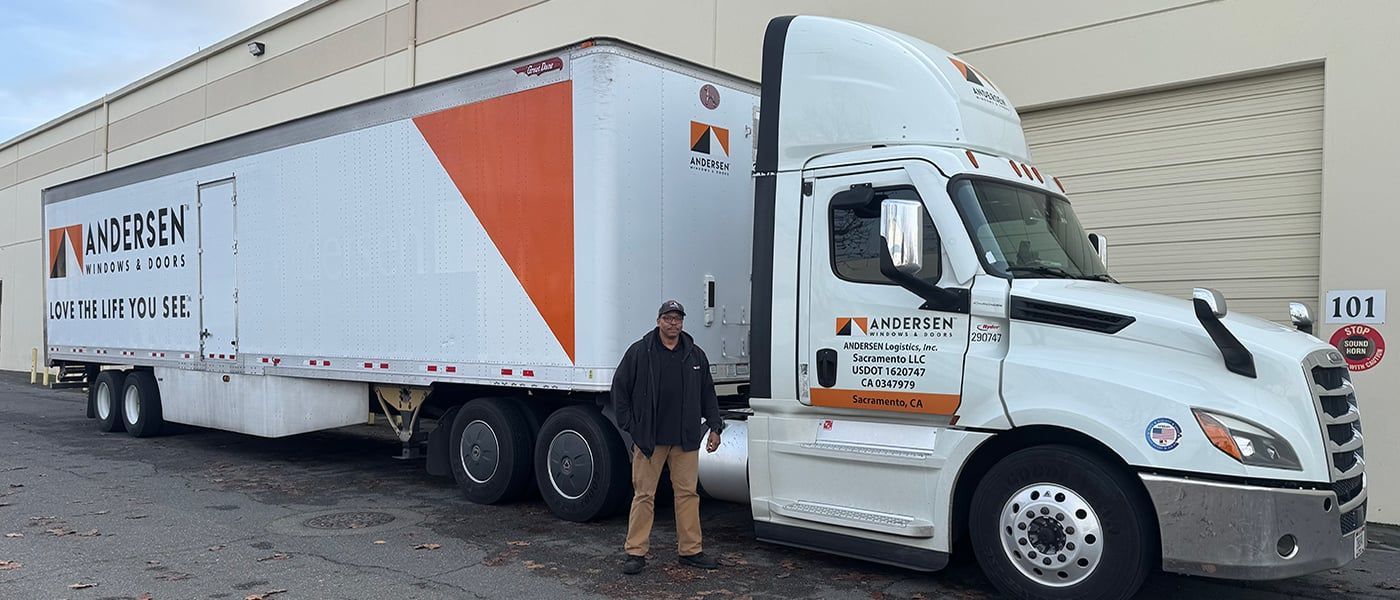 White pickup truck carrying large sheets of glass, secured with ropes, on a city street.