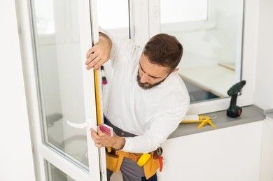 Construction worker sealing a window with foam. Wearing hard hat, safety vest, and gloves. Sunny outdoor setting.