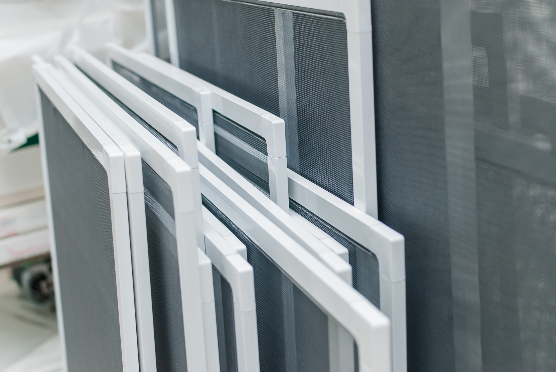 Stack of white-framed window screens with gray mesh.