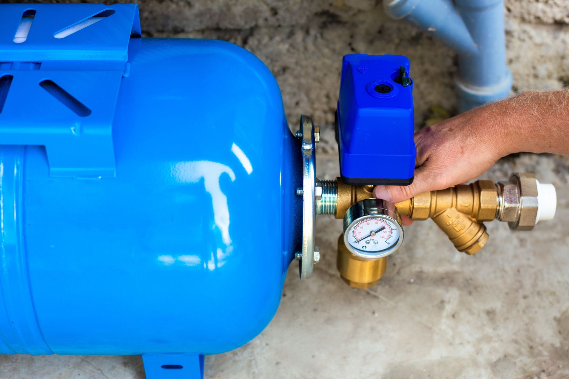 Hand adjusts the pressure gauge on a blue household water pump system.