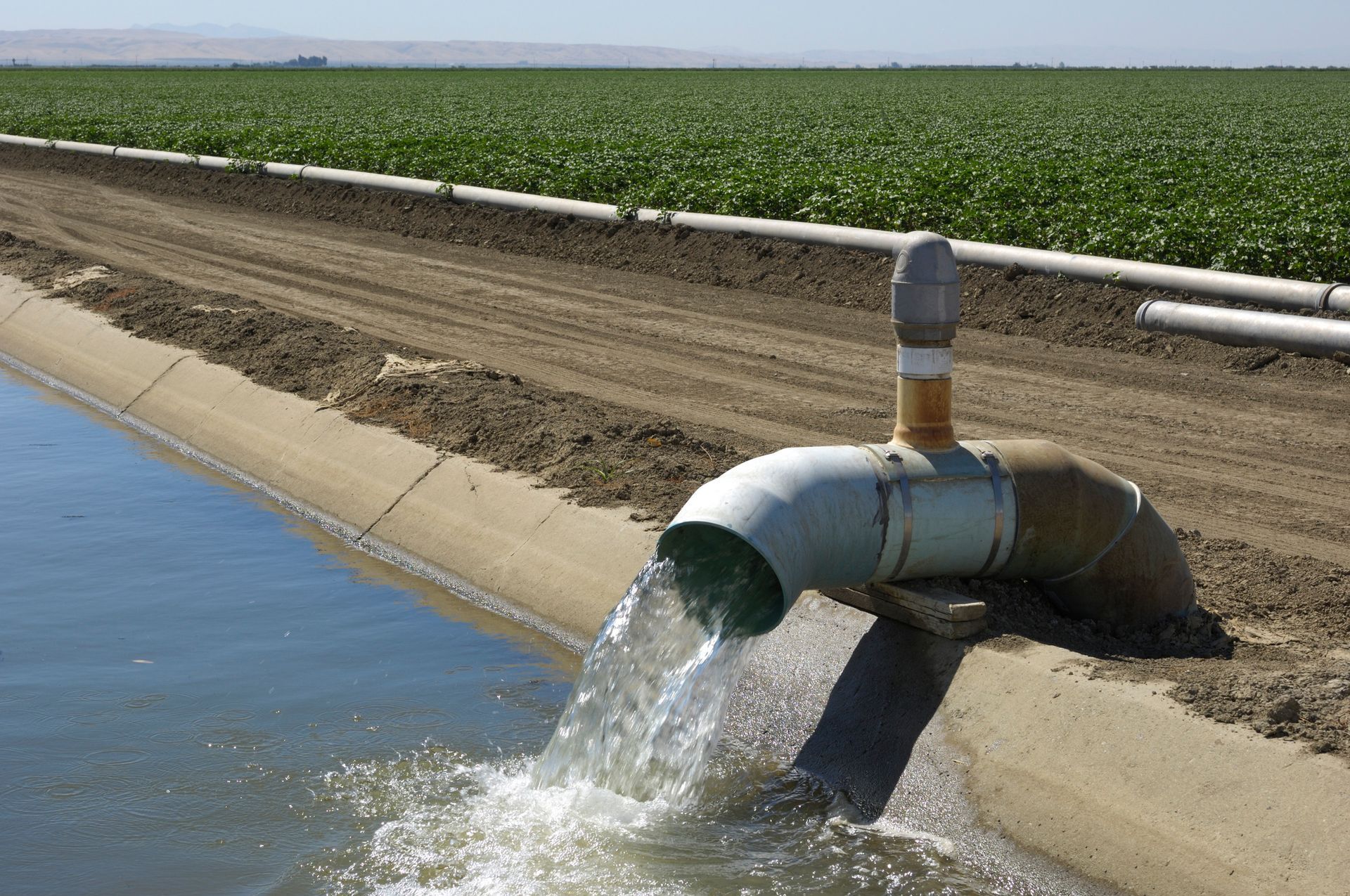 On a farm, a pipe is leaking water, highlighting the importance of water well system repair.