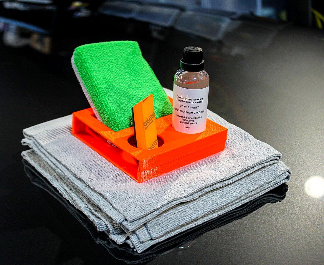 A bottle of professional ceramic coating, green applicator pad sitting on top of microfiber towels