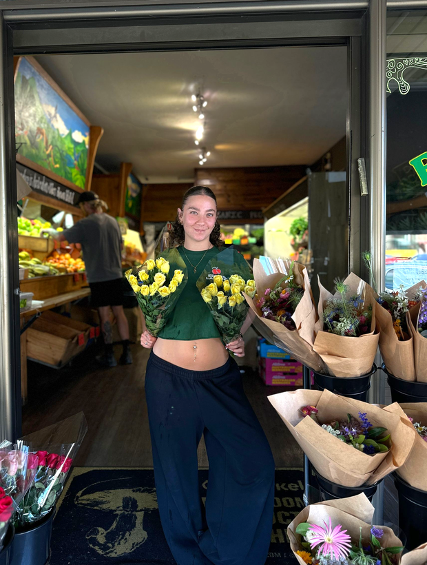 Edens Landing Staff member holding fresh local roses at the entrance of organic grocer in Mullumbimby, Northern Rivers