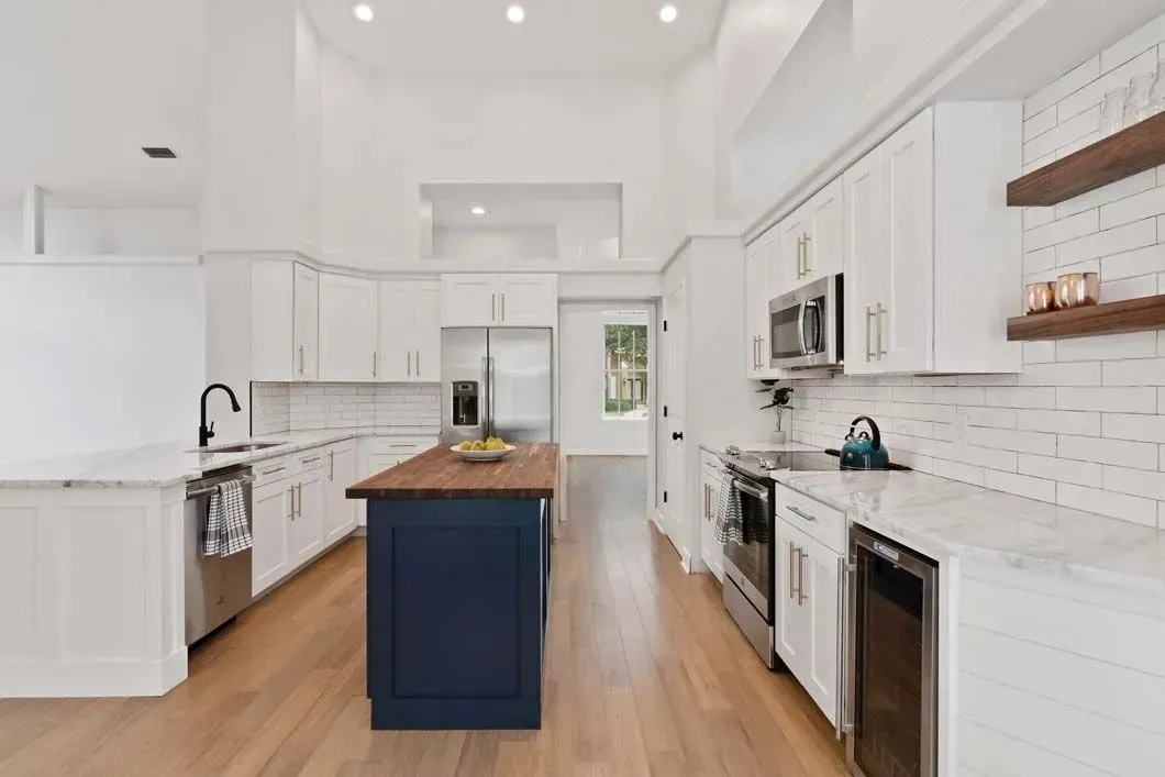 A kitchen with white cabinets , stainless steel appliances , and a blue island.