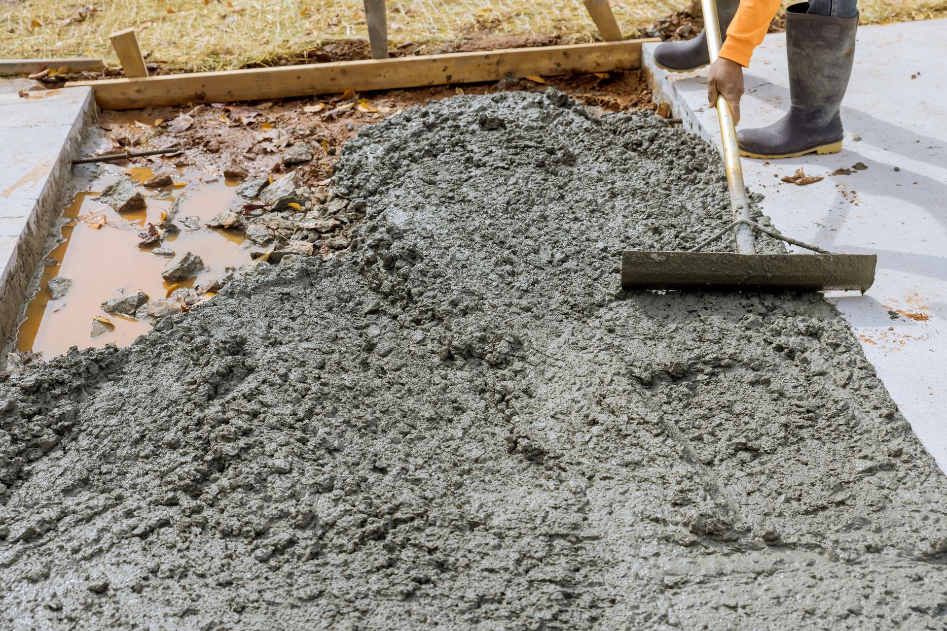 A person is spreading concrete on a sidewalk with a rake.