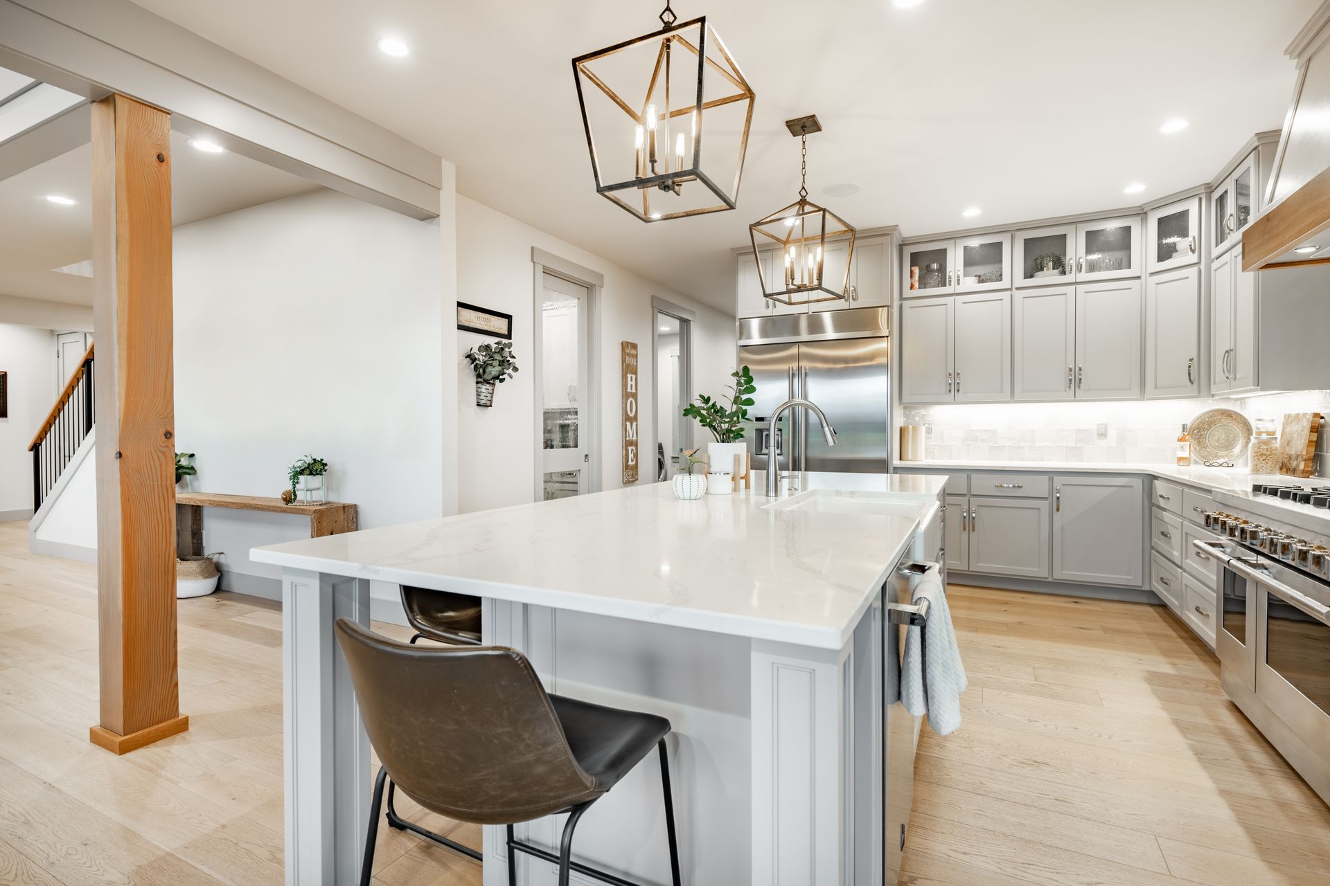 A kitchen with white cabinets , stainless steel appliances , a large island and a chair.