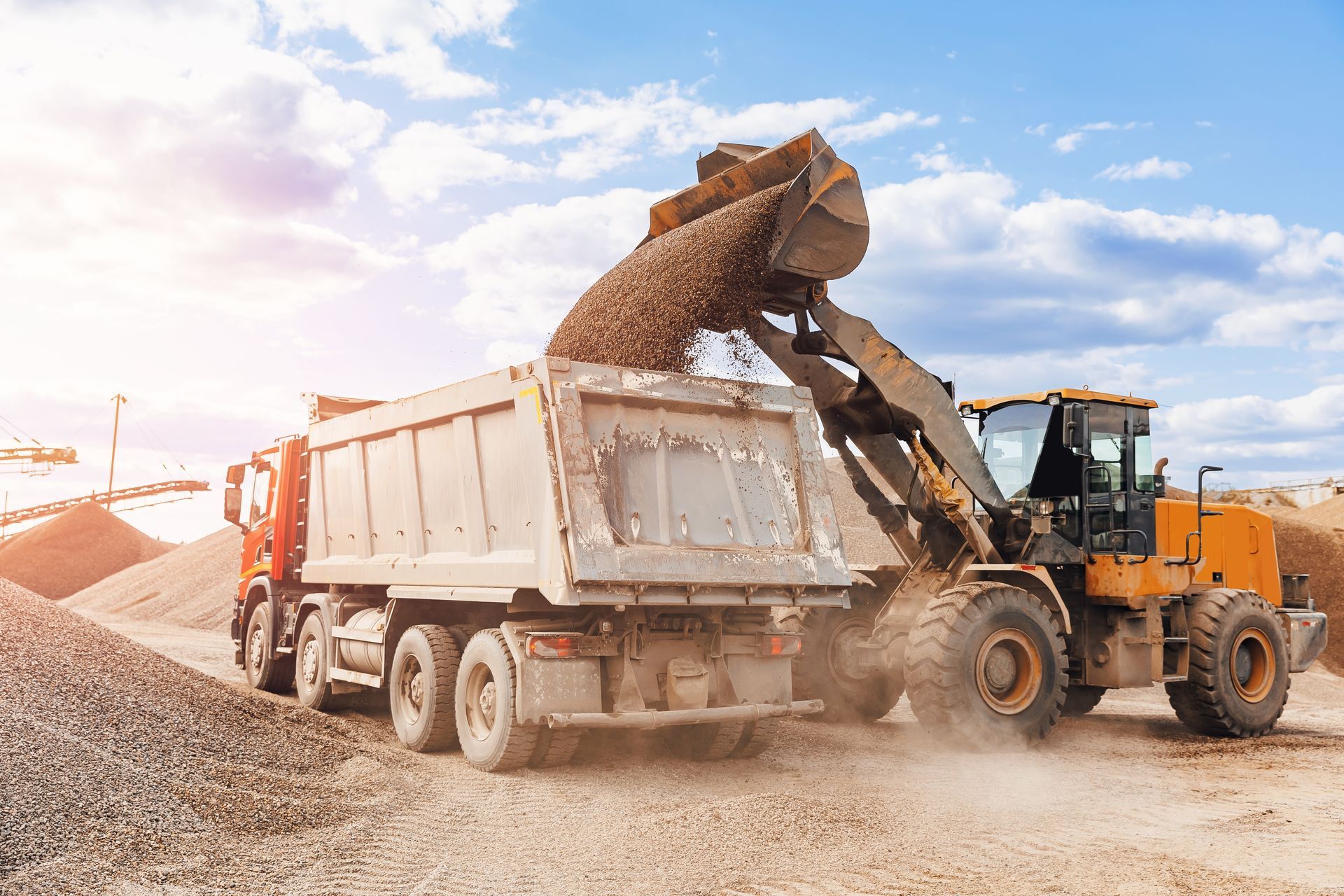 A dump truck is being loaded with gravel by a bulldozer.