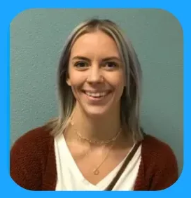 Woman with blonde-streaked hair, smiling, wearing a white shirt and brown cardigan, against a blue wall.