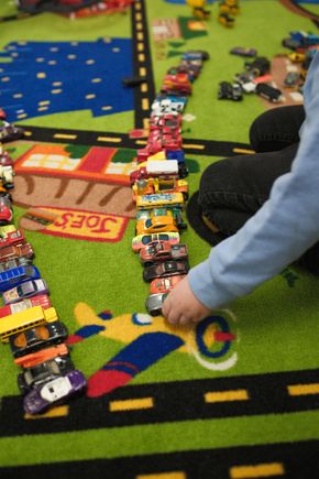 Family of four embraces in a park. Woman in brown jacket smiles, surrounded by three children.