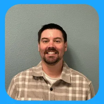 Man with a beard smiling, wearing a plaid shirt, against a blue background.