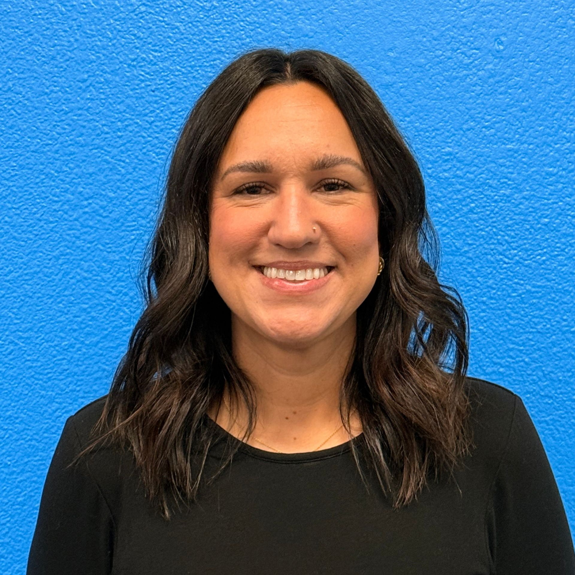 Blond woman smiling, wearing a light-colored top, in front of a bookshelf.