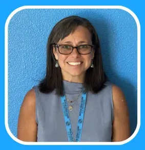 Woman with glasses smiling, wearing a blue lanyard, in front of a blue wall.