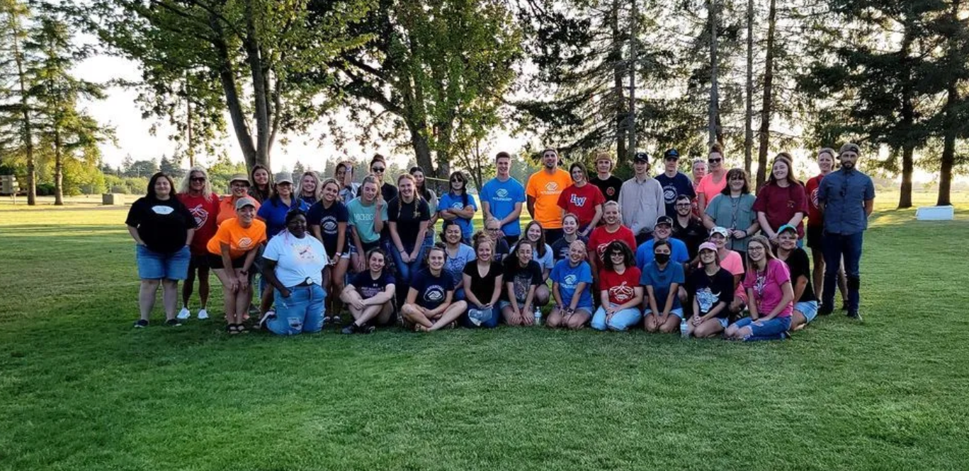 Happy family of four smiles outside; parents giving children piggyback rides.