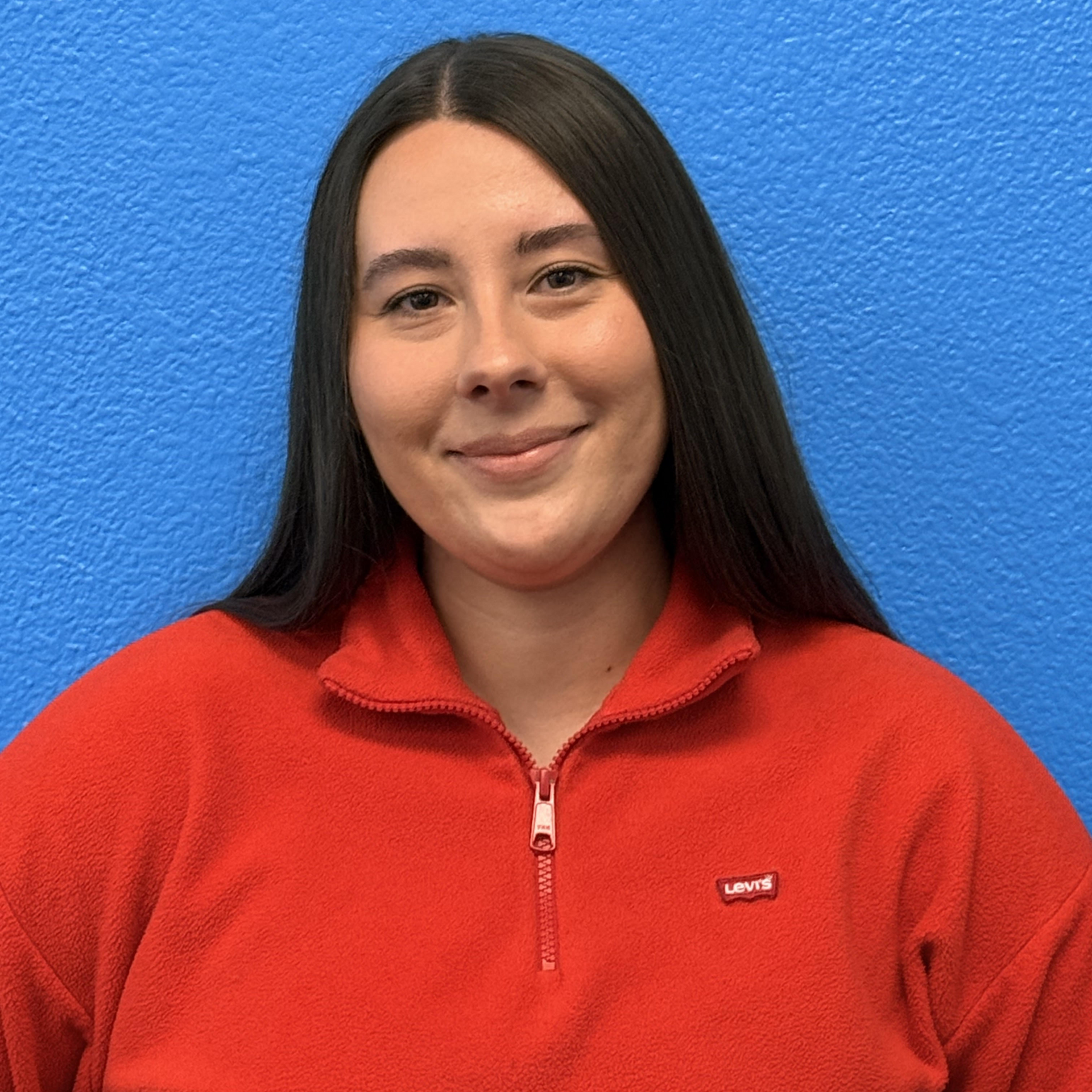 Blond woman smiling, wearing a light-colored top, in front of a bookshelf.