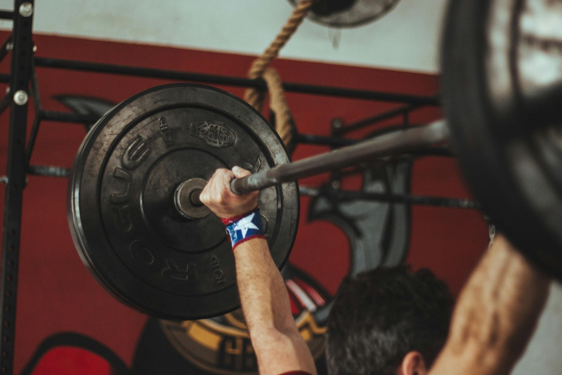 Man lifting a barbell with weights at a gym, wearing a blue and white wristband, indoors.