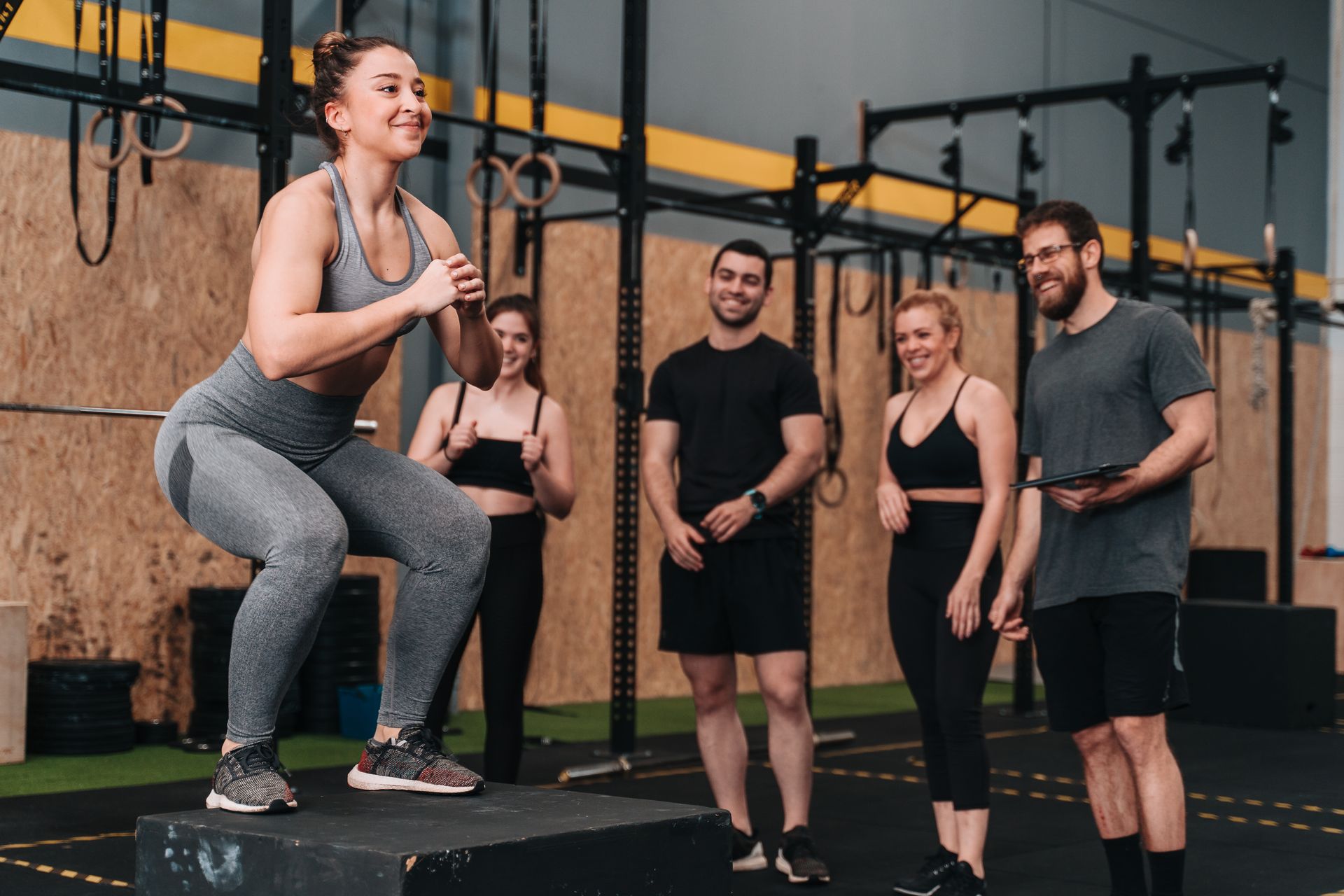 Woman doing box jumps at a gym with friends, smiling.